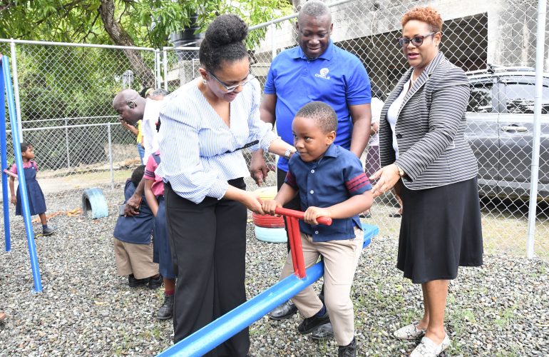 Claudine Allen (left), General Manager of the JN Foundation, helps a student of Chapel Hill Basic School enjoy the seesaw, as Norman Hinds, President of the JN Circle Morant Bay chapter, and Nina Peters, Business Relationship and Sales Manager at JN Bank, look on with smiles.